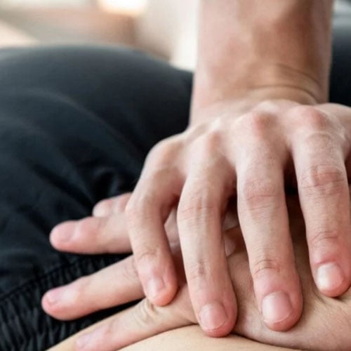 A close-up of hands performing a massage, with one hand placed on top of another on the back of a person.