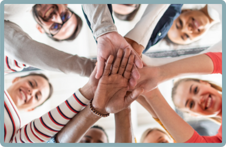 A group of people with their hands stacked in the center, forming a circle. They are smiling, and the image is taken from above, showing their faces and hands. The group includes both men and women, with diverse skin tones.