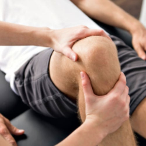 A close-up image of hands performing a therapeutic treatment on a person's knee. One hand is holding the knee while the other is applying pressure.